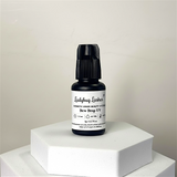 Bottle of Ladybug Lashes Dew Drop UV on a white hexagonal platform with a plain background